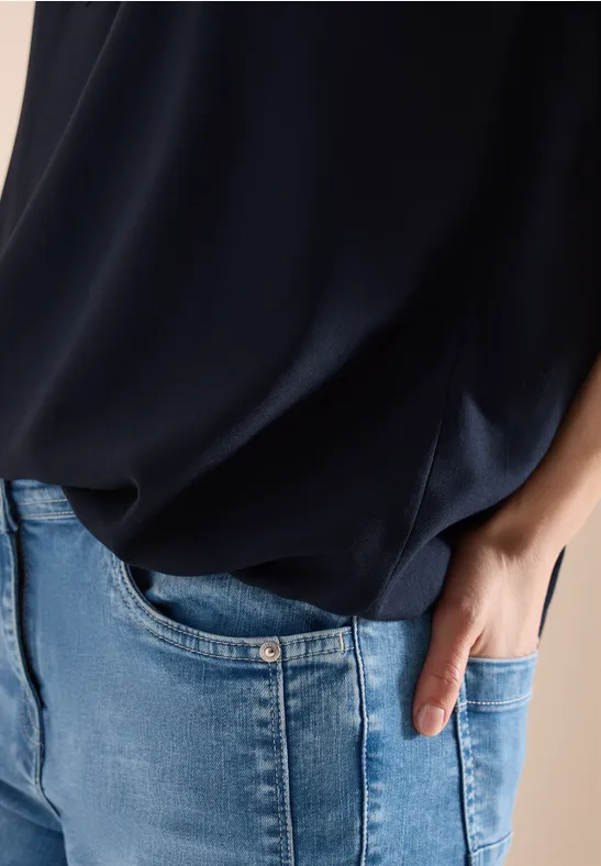 Nahaufnahme einer Person in dunkelblauem Oberteil und hellblauer Jeans, Hand locker in der Hosentasche