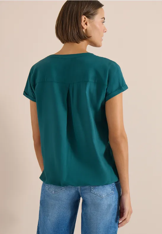 Eine Frau von hinten in einem grünen T-Shirt und blauen Jeans.