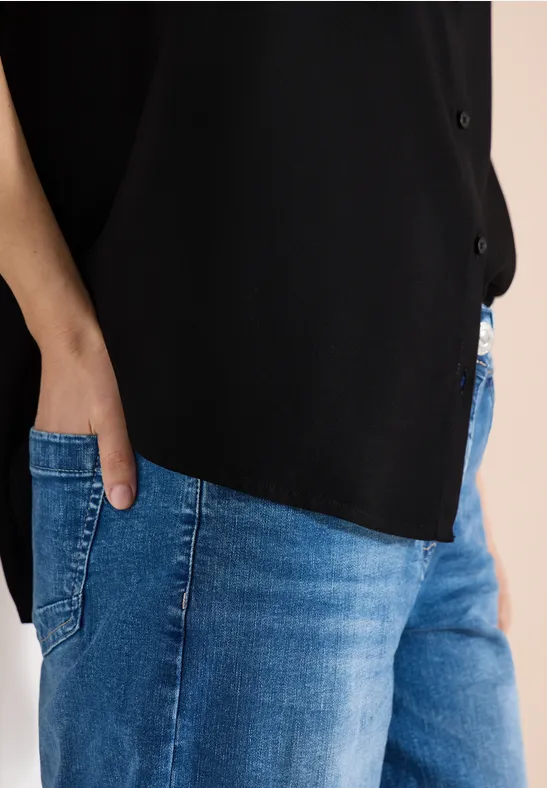 Nahaufnahme einer Person mit Hand in der Jeans-Tasche, trägt blaue Jeans und schwarzes Oberteil.