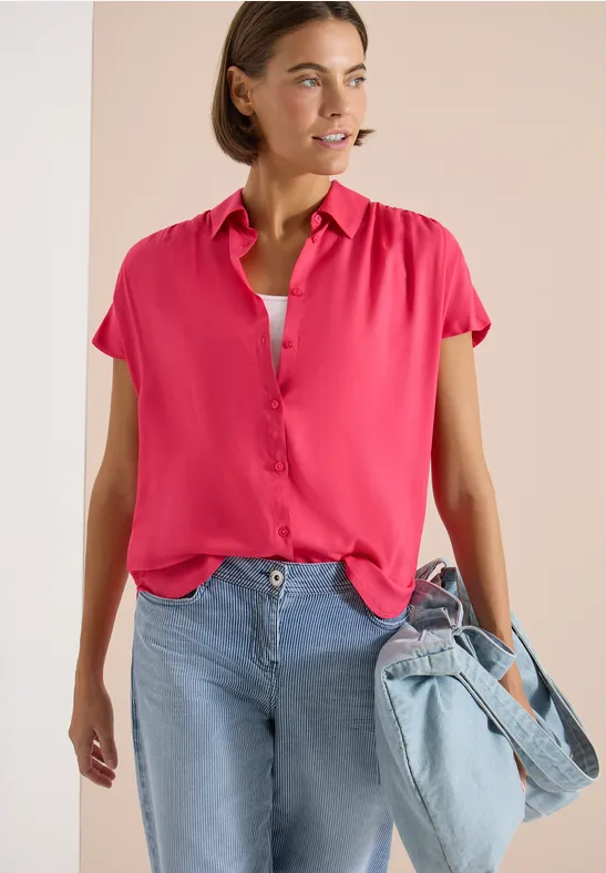 Frau in pinker Bluse, Jeans und einer Jeans-Tasche.