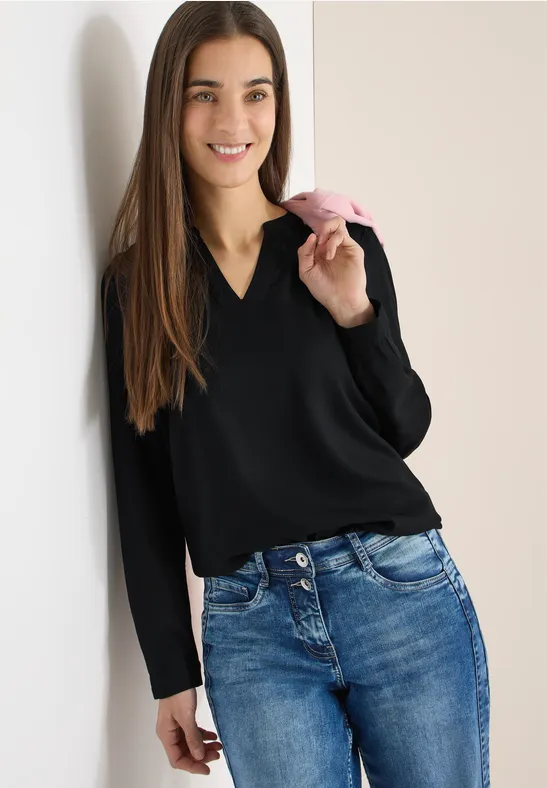 Frau in schwarzem Pullover und Jeans isst Eis am Stiel.