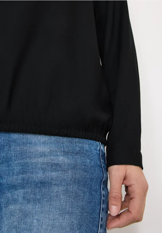 Person trägt schwarze Bluse mit Gummizug am Saum und blaue Jeans.