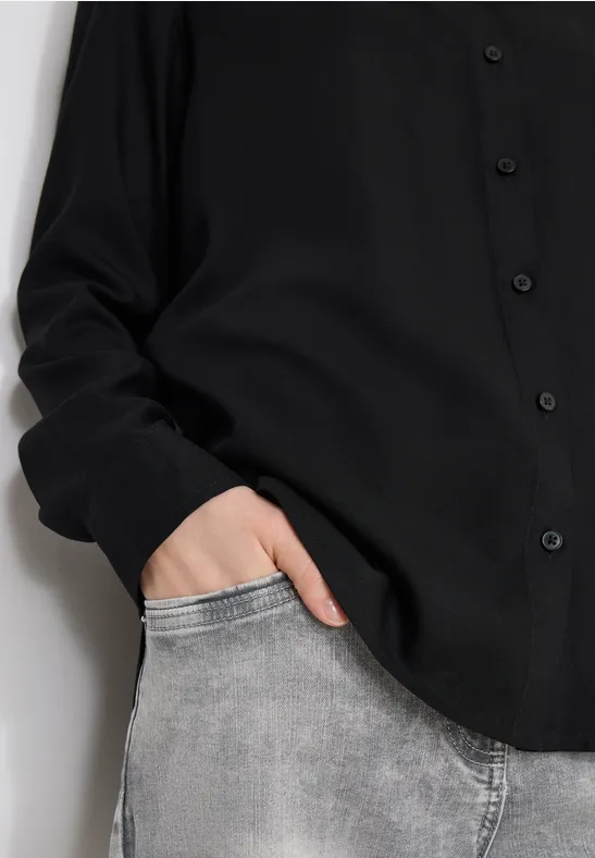 Person trägt schwarzes Hemd, hat die Hand in der vorderen Tasche ihrer grauen Jeans.