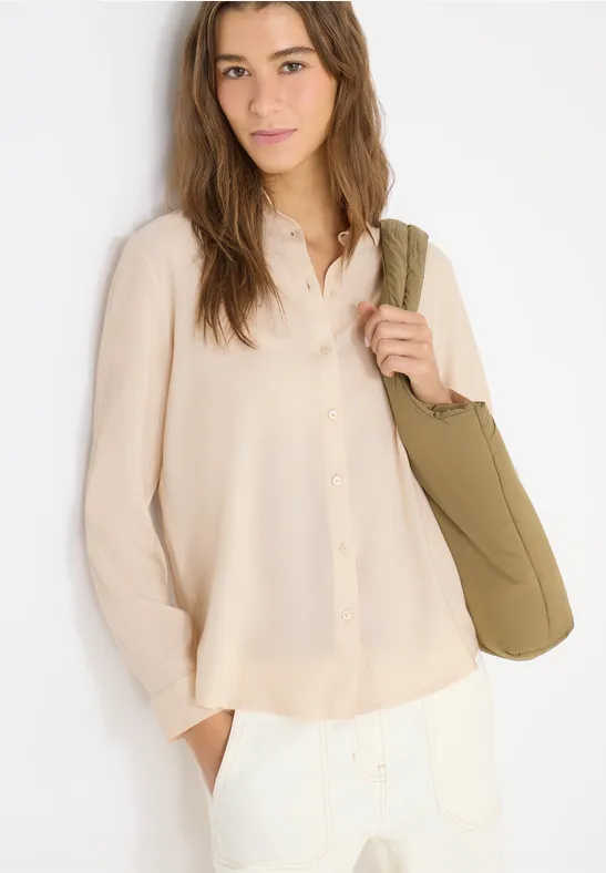 Frau in cremefarbener Bluse und weißer Hose mit grüner Tasche.