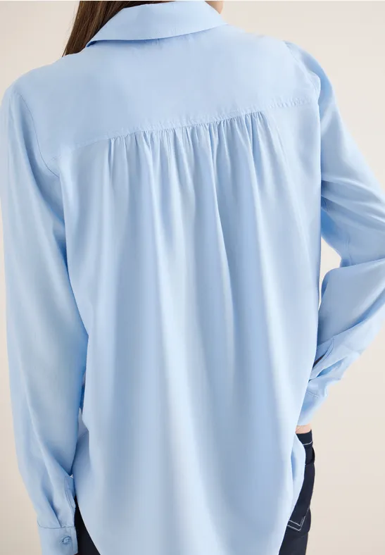 Frau von hinten in hellblauer Bluse mit langen Ärmeln
