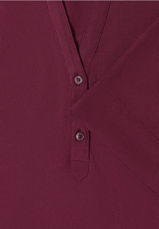 Nahaufnahme eines weinroten V-Ausschnitt-Oberteils mit Knopfleiste.