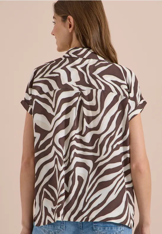 Femme vue de dos portant un chemisier à manches courtes avec motif zèbre marron et blanc.