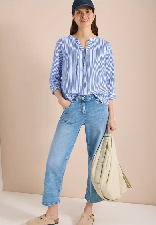 Frau in hellblau-weiß gestreiftem Hemd, leger in gerade Jeans gesteckt, mit großer beigefarbener Stofftasche.