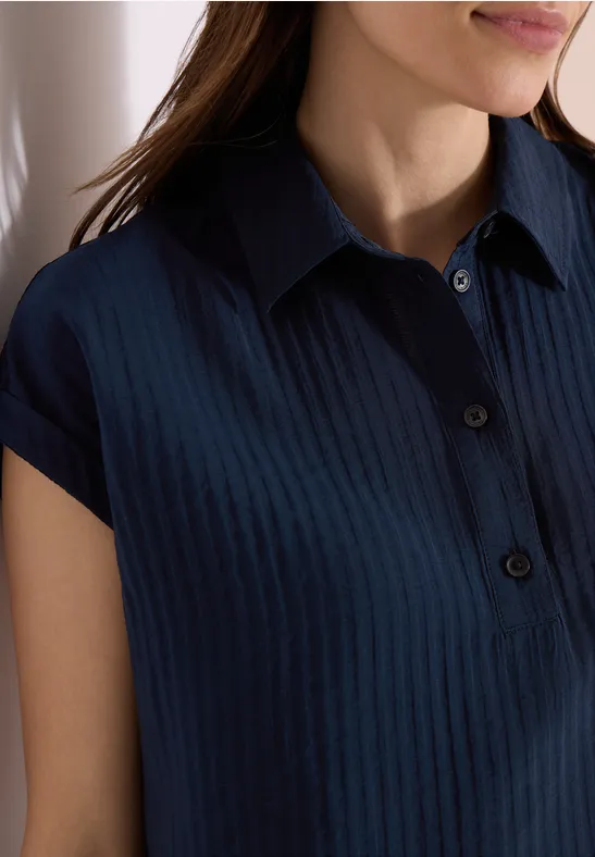 Eine Frau trägt ein dunkelblaues, geripptes Poloshirt mit kurzen Ärmeln.