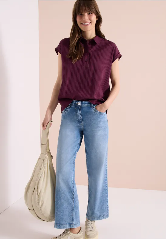 Dame trägt lila Bluse, Jeans, hält Tasche.