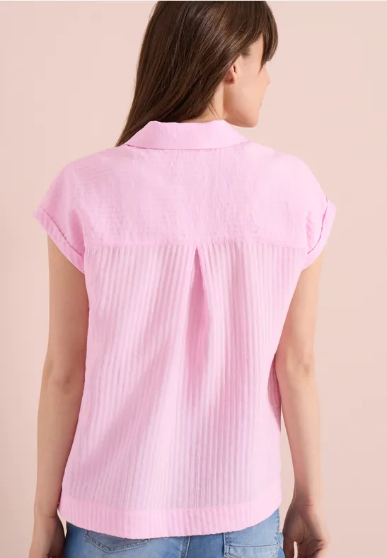 Femme de dos en chemise rose à manches courtes, col chemisier et pli au dos.