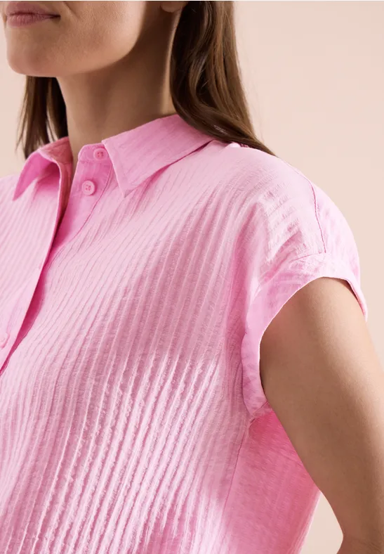 Femme en chemise rose texturée à manches courtes et col classique, vue de côté sur fond clair.