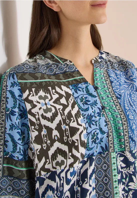 Nahaufnahme einer Frau in blau-grüner, gemusterter Bluse.