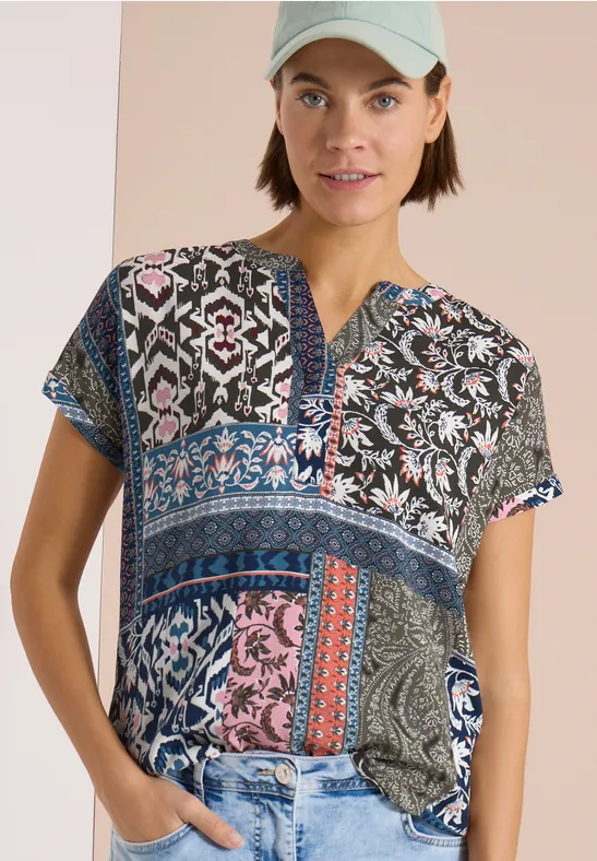 Person trägt bunt gemusterte Patchwork-Bluse mit floralen und grafischen Motiven