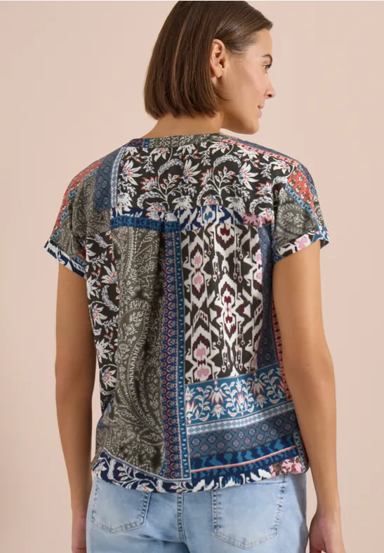 Frau von hinten trägt gemustertes Kurzarmshirt und helle Jeans.