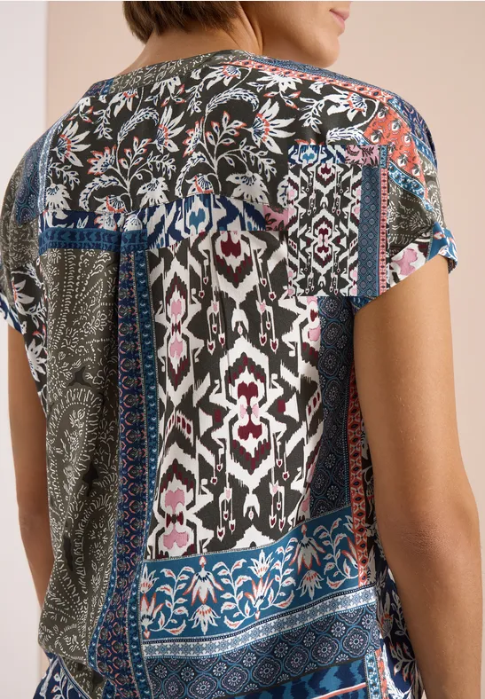 Frau von hinten in kurzärmeligem, buntem Patchwork-Oberteil mit floralen und geometrischen Mustern.