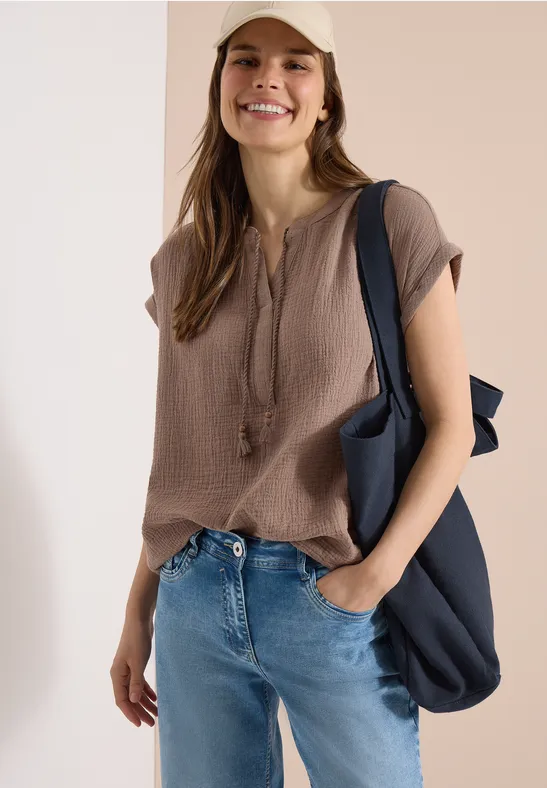 Eine Frau trägt ein kurzärmliges braunes Oberteil, Jeans und eine blaue Umhängetasche.