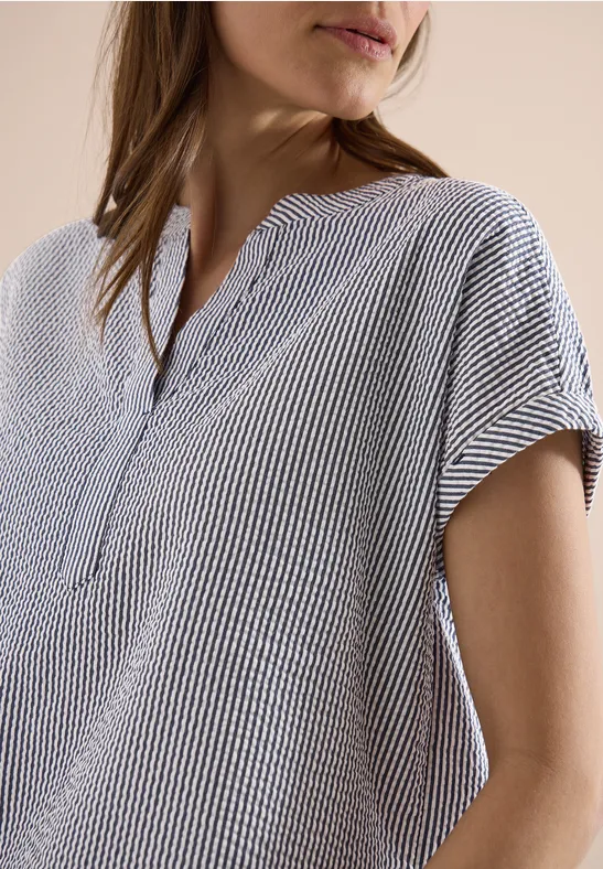 Eine Person trägt eine kurzärmlige Bluse mit weiß-schwarzen Streifen, V-Ausschnitt und Knopfleiste.