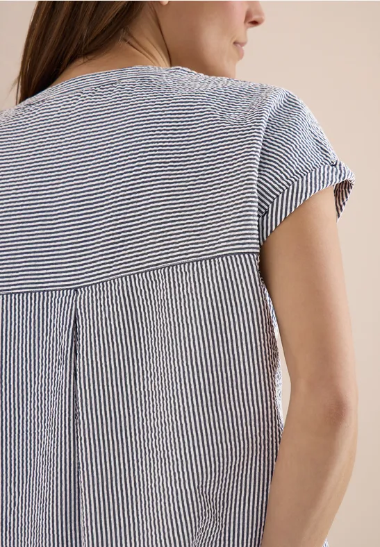 Rückansicht einer Frau in kurzärmeligem, blau-weiß gestreiftem Oberteil.