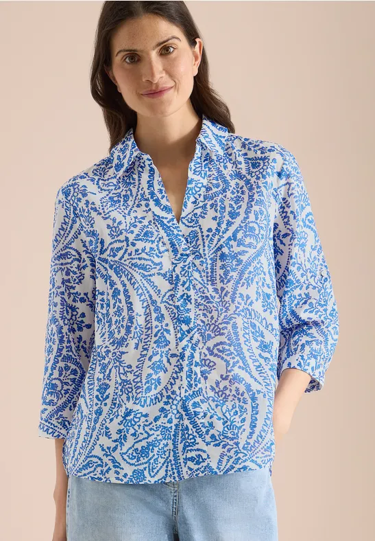 Frau trägt blau-weiß gemusterte Paisley-Bluse mit 3/4-Ärmeln.