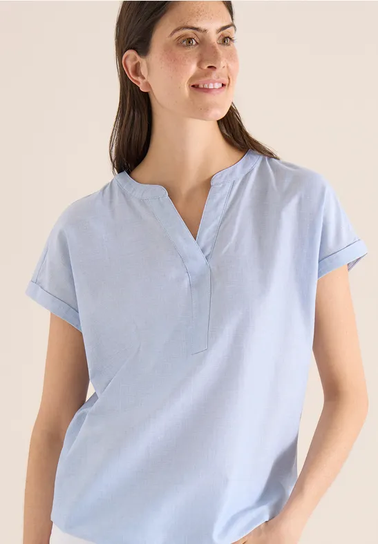 Frau trägt hellblaues, kurzärmeliges, locker sitzendes Shirt mit V-Ausschnitt.