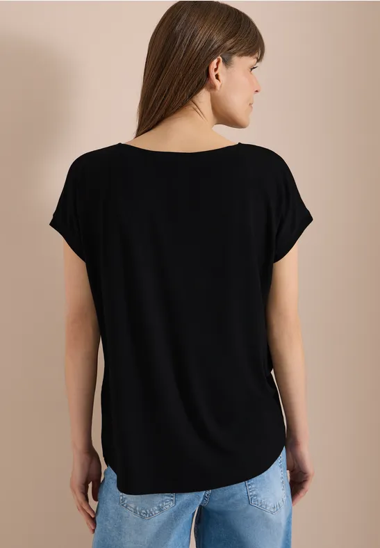 Vue de dos d'une personne portant un t-shirt noir ample et un jean bleu clair sur fond neutre.