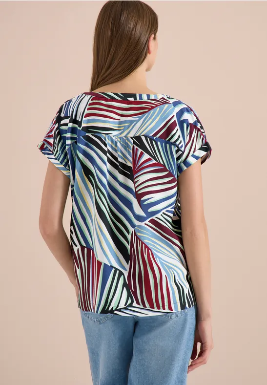 Femme de dos portant un haut ample à rayures colorées à manches courtes, associé à un jean bleu.