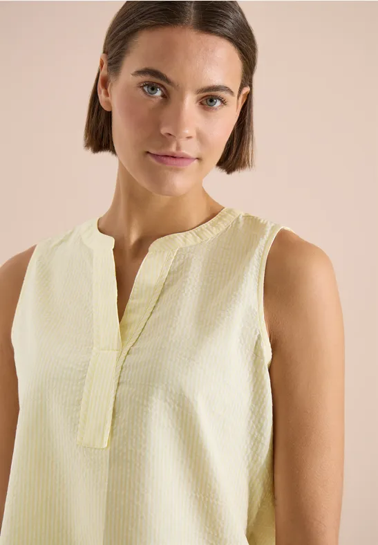 Femme portant un top sans manches jaune pastel sur fond neutre.