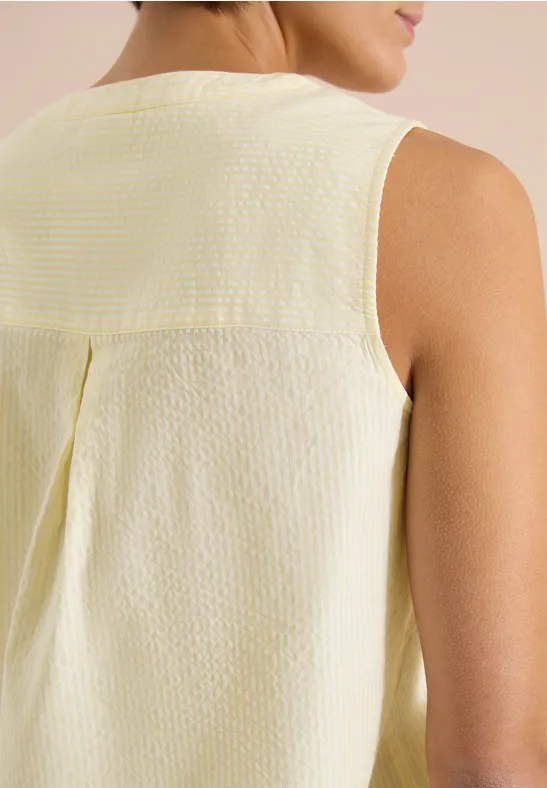 Gros plan du dos d’une femme portant un top sans manches texturé jaune pâle et blanc.