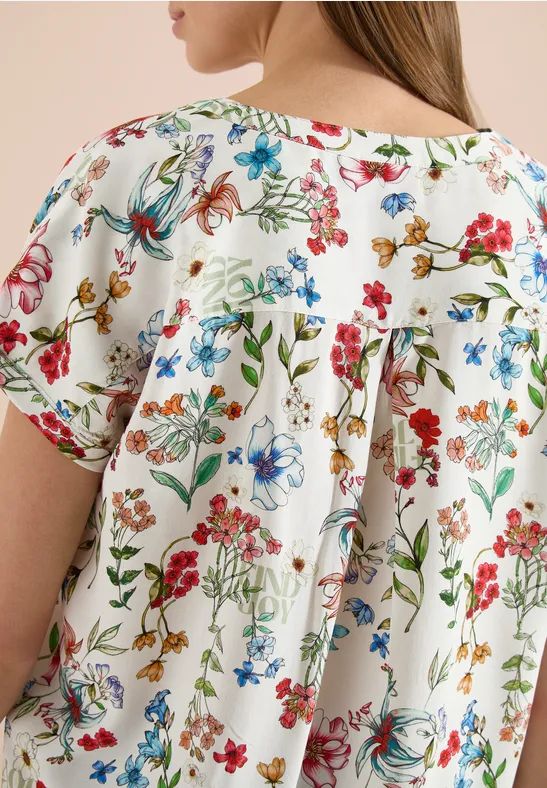Nahe Ansicht einer weißen Bluse mit buntem Blumenprint und lockerem, gerafftem Rückendetail.