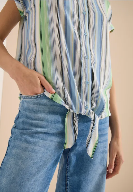 Nahaufnahme einer Person in gebundenem gestreiftem Hemd und blauen Jeans, Hand steckt in Hosentasche.