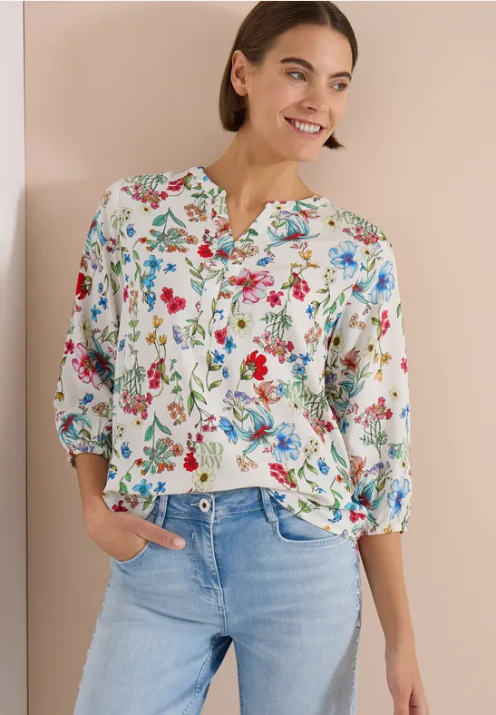 Frau trägt weiße Bluse mit buntem Blumenmuster und hellblaue Jeans