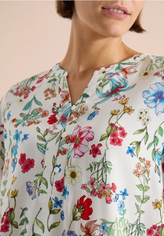 Frau trägt weiße Bluse mit buntem Blumenmuster und V-Ausschnitt.