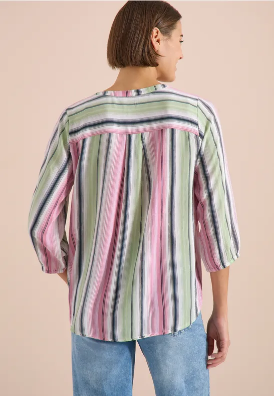 Vue de dos d'une personne portant une chemise ample à rayures verticales colorées et un jean bleu.
