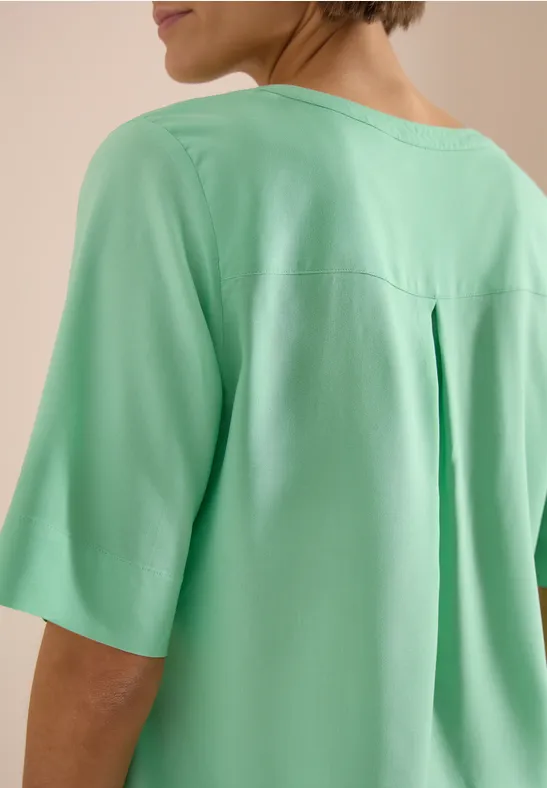 Femme vue de dos portant un haut vert clair à manches mi-longues.
