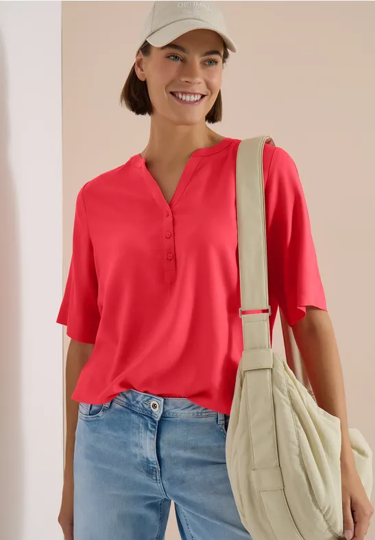 Femme en chemisier rouge, jean bleu et sac besace beige.
