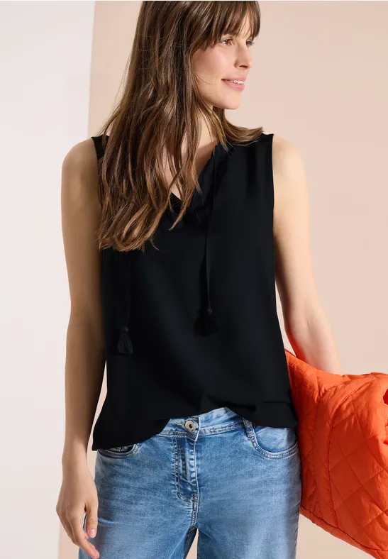 Femme portant un top noir sans manches, jean bleu clair et une veste matelassée orange négligemment sur le bras.