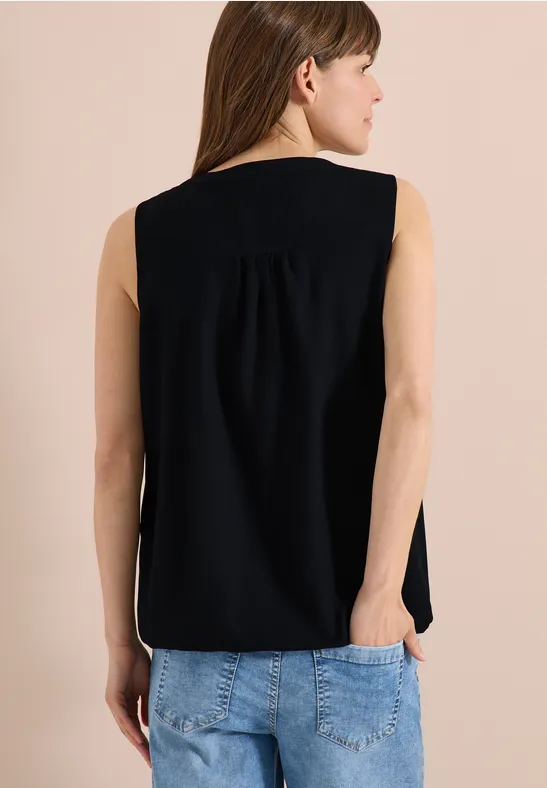 Femme de dos portant un haut noir sans manches et un jean bleu, mains dans les poches.