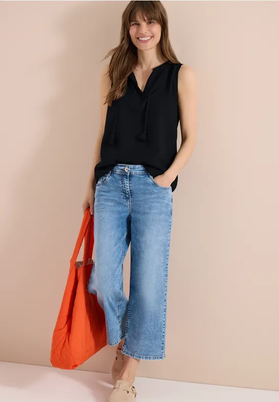 Femme portant un jean large bleu et un débardeur noir, avec un sac orange sur fond beige.