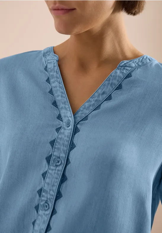 Haut bleu clair à col V avec volants décoratifs le long de la patte de boutonnage.