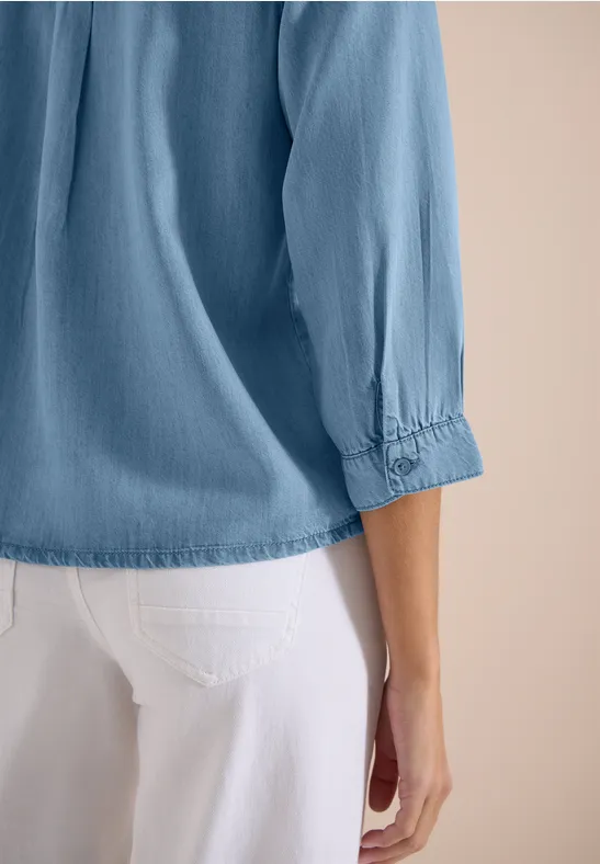 Vue arrière latérale d'une personne portant une blouse bleu clair à manches 3/4 et un pantalon blanc.