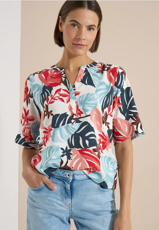 Femme en chemisier coloré à motif tropical et jean clair.
