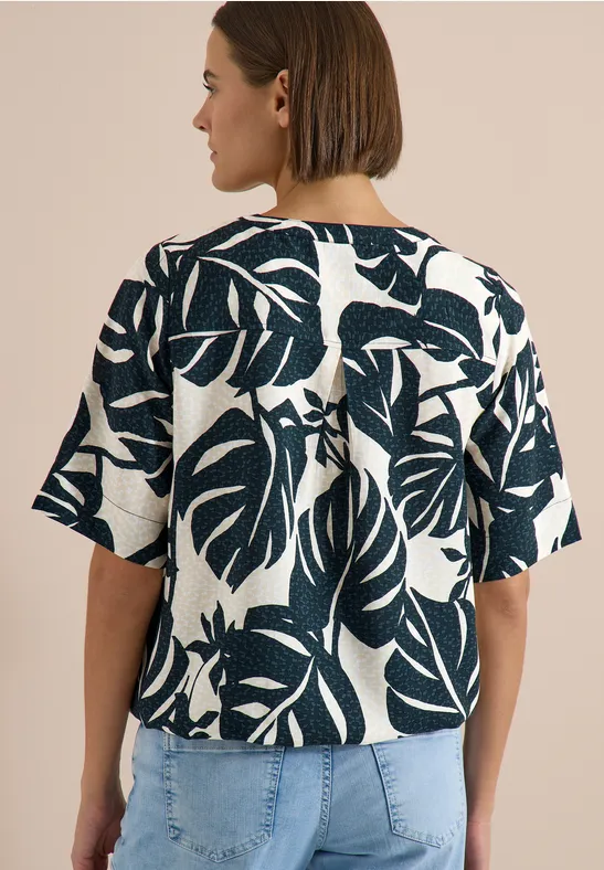 Vrouw van achteren in jeans en wit kort mouw top met groot donkergroen bladprint.