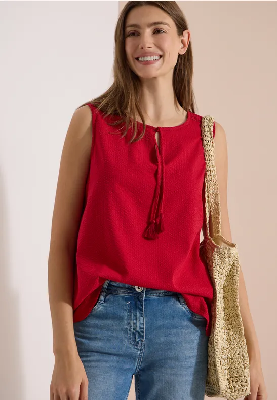 Femme en top rouge sans manches, jean et sac cabas beige à motif.