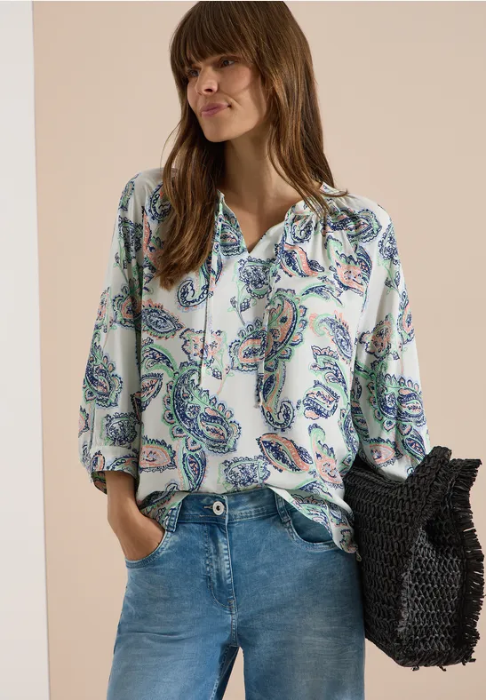 Femme en jean et chemise à imprimé paisley, portant un sac filet noir.