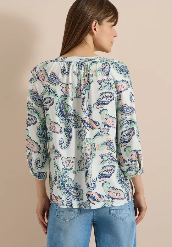 Vue de dos d'une femme portant un chemisier clair à motifs paisley et un jean bleu.