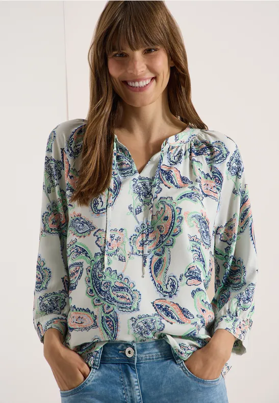 Une femme porte un chemisier ample à motif paisley coloré et encolure en V.