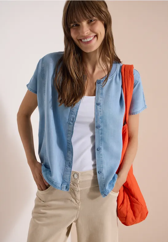 Person trägt weißen T-Shirt, offene Jeansbluse, beige Hose und orange Umhängetasche.