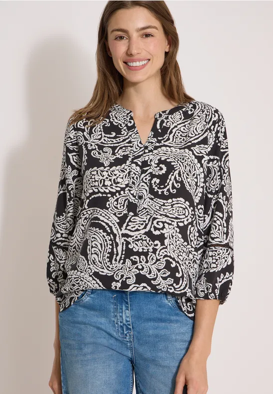 Une femme porte un chemisier noir et blanc à motifs et un jean bleu.