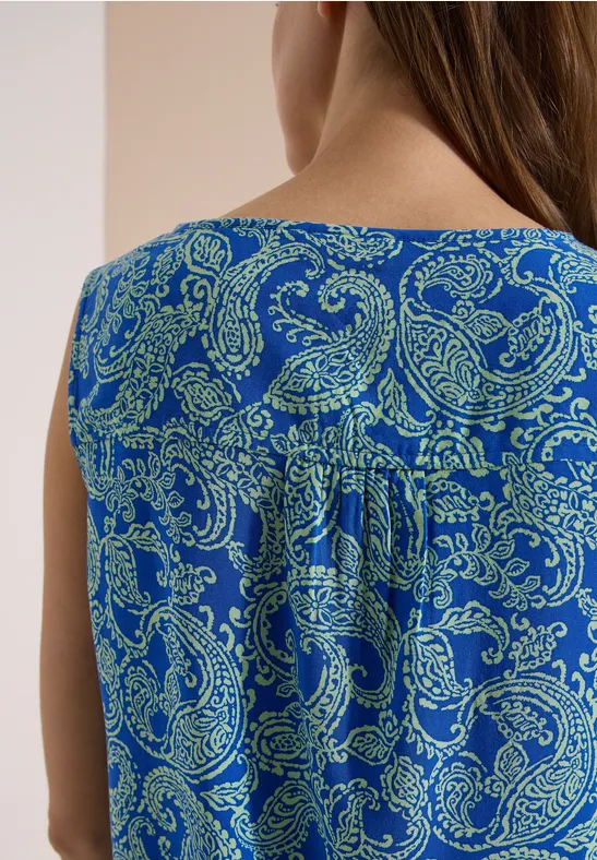 Rückansicht einer Person in ärmellosem, blauem Oberteil mit grünem Paisley-Muster.